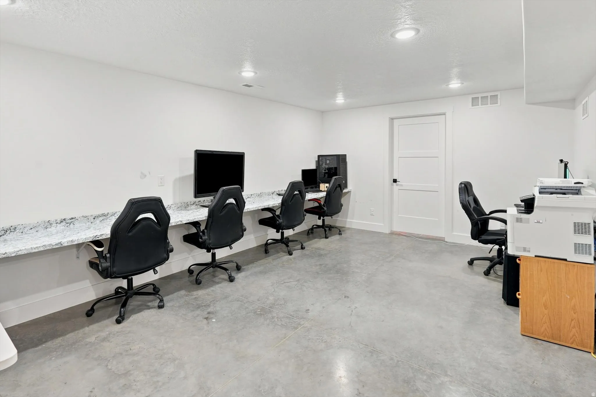 Spacious room featuring a long built-in countertop with a speckled stone finish, concrete flooring, recessed lighting, and white walls