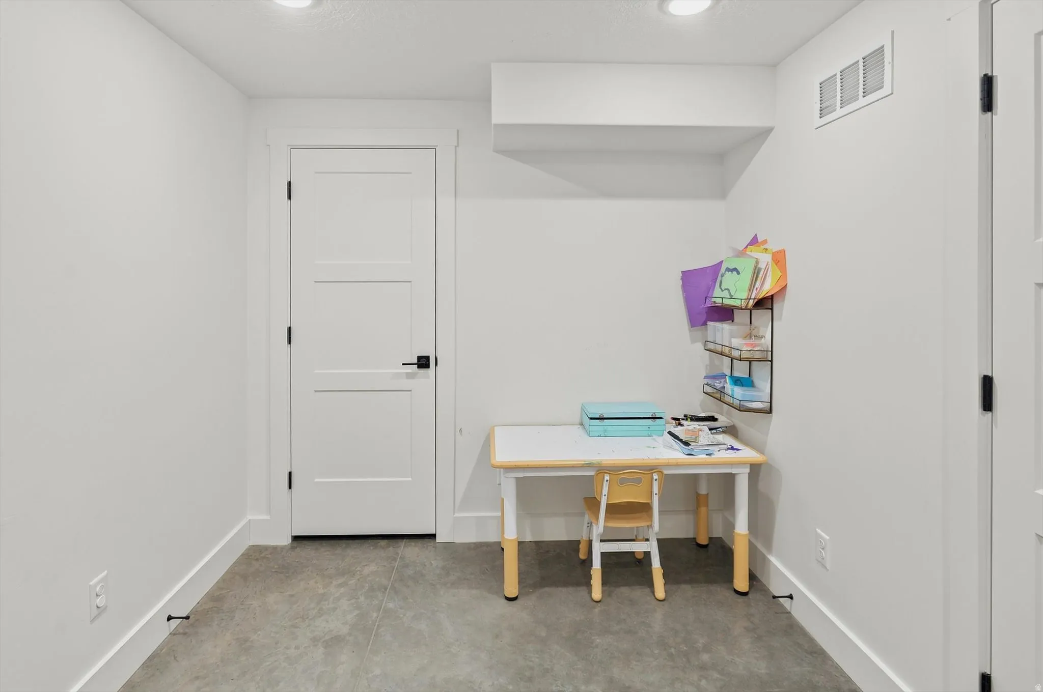 Spacious room featuring light gray flooring, recessed lighting, white trim, and a white three-panel door with black hardware