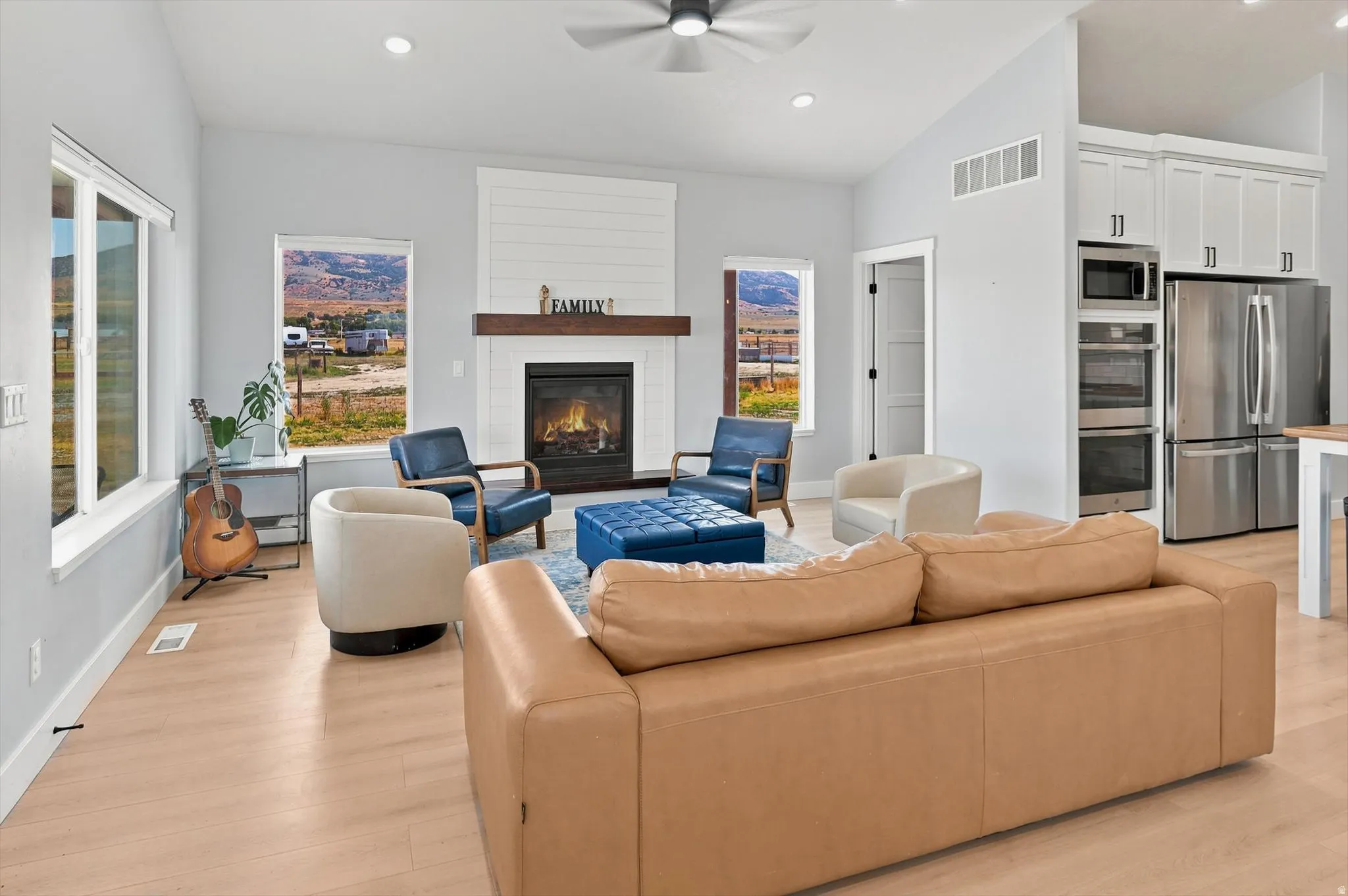 Open-concept living space featuring a fireplace with a wood mantel, light wood-finish flooring, recessed lighting, and a ceiling fan