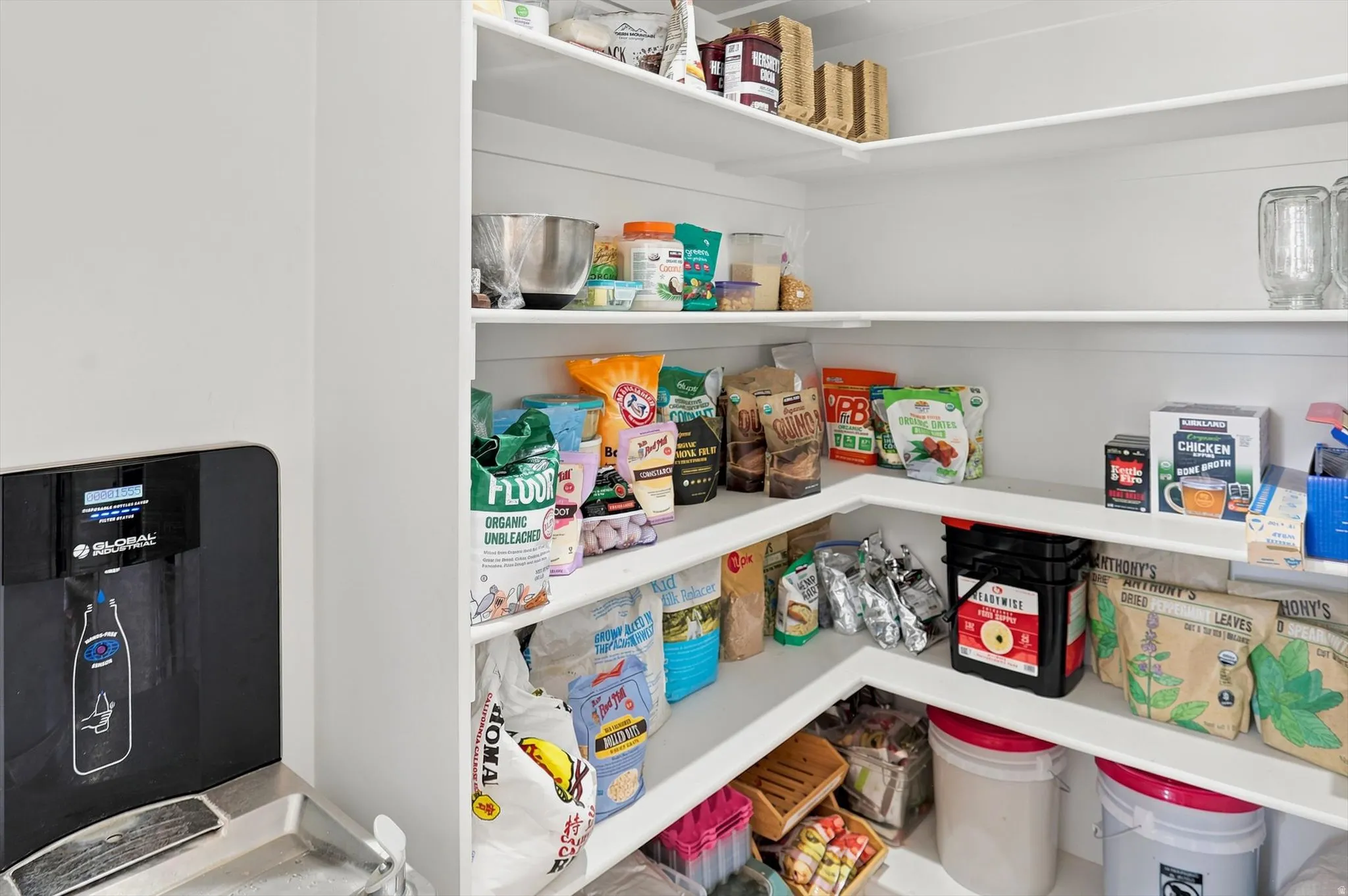 Spacious pantry featuring extensive wrap-around shelving, a built-in water dispenser, and bright white wall finishes