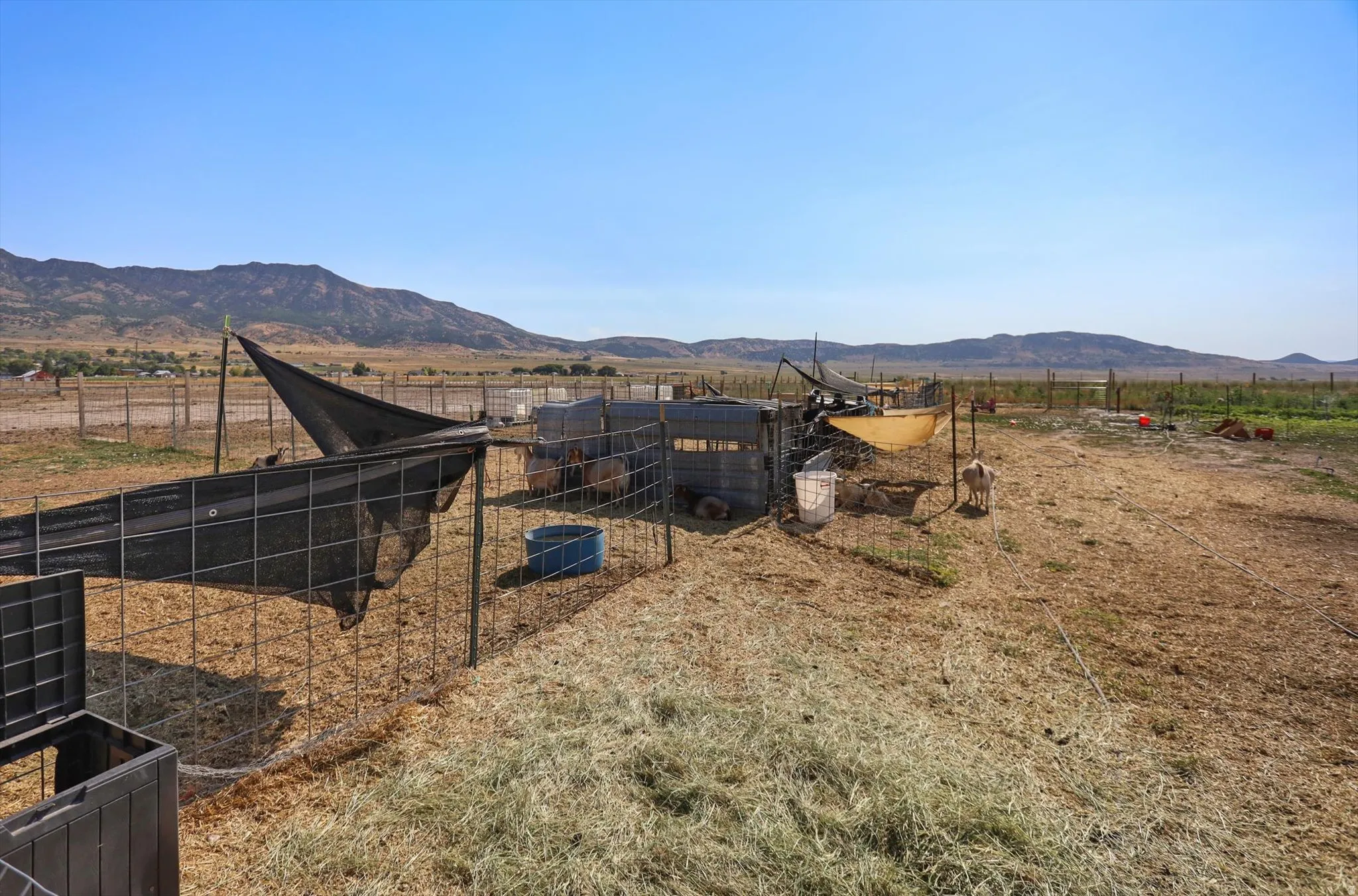 Expansive open land featuring fencing, a shade structure, and distant mountain scenery
