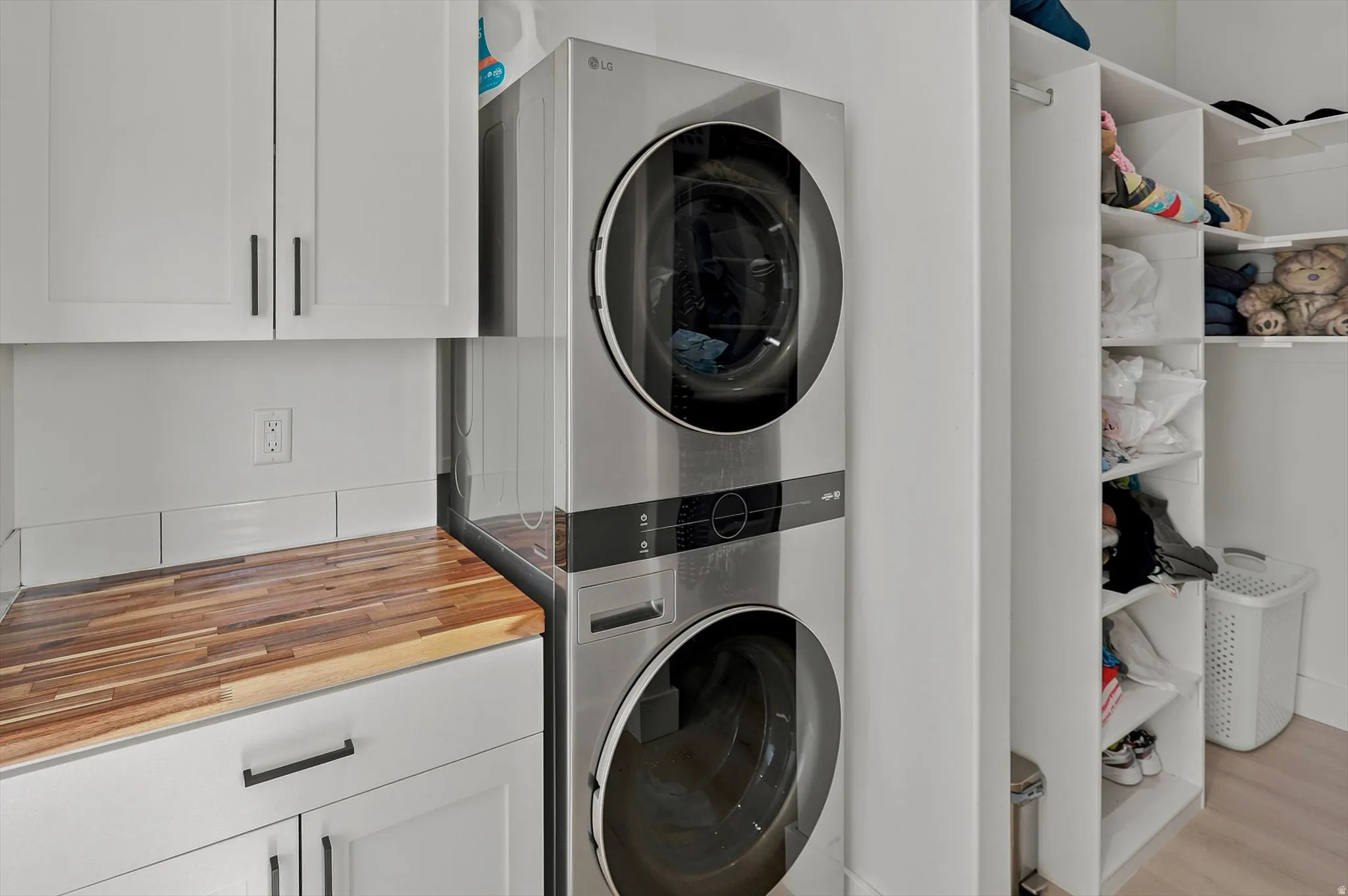 Laundry area featuring a stacked washer and dryer, white shaker cabinetry with dark hardware, a wood-finish countertop, and built-in shelving
