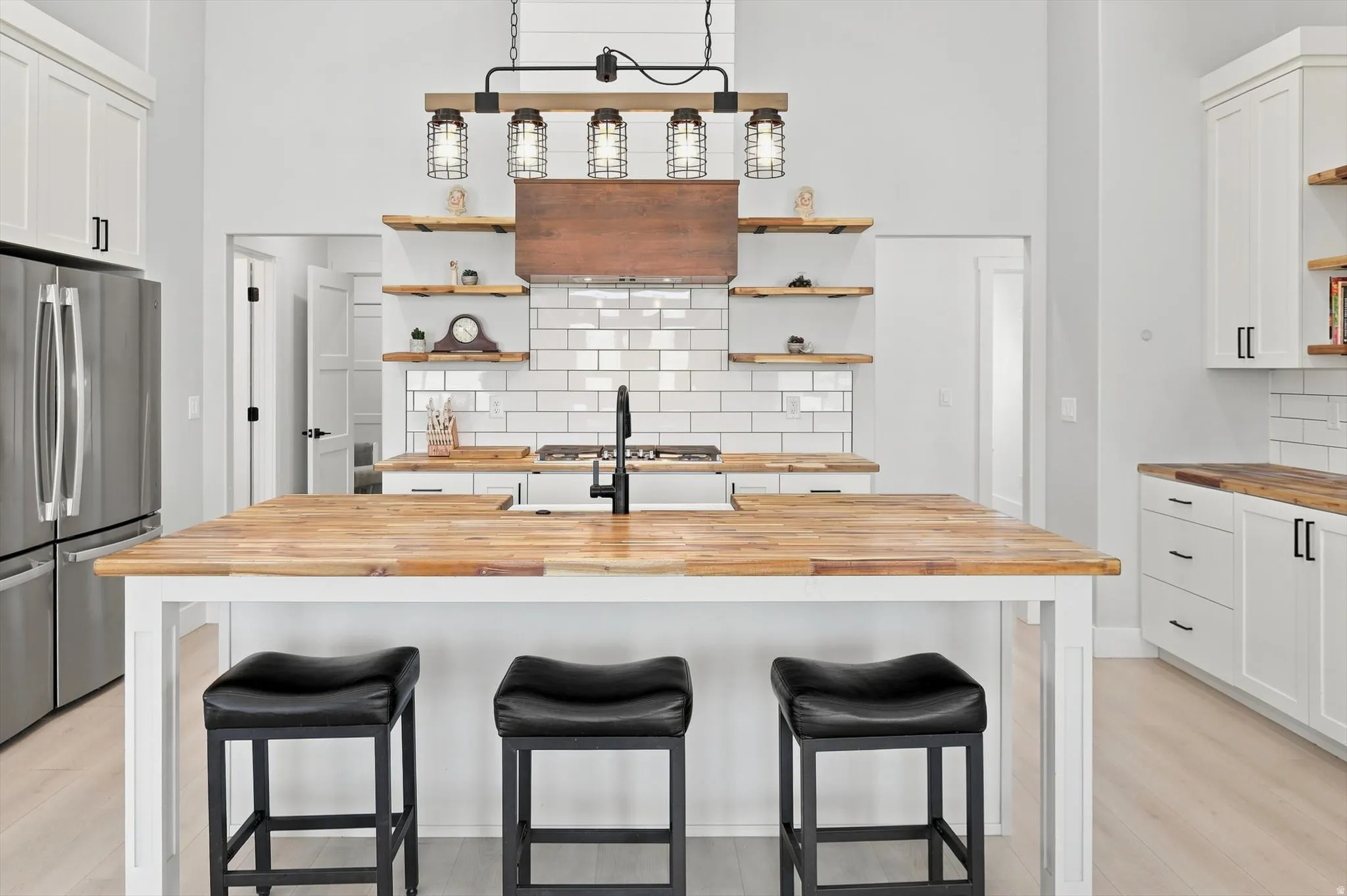 Kitchen featuring a large wood-finish island, white subway tile backsplash, a stainless steel refrigerator, white cabinetry, and a unique industrial-style chandelier