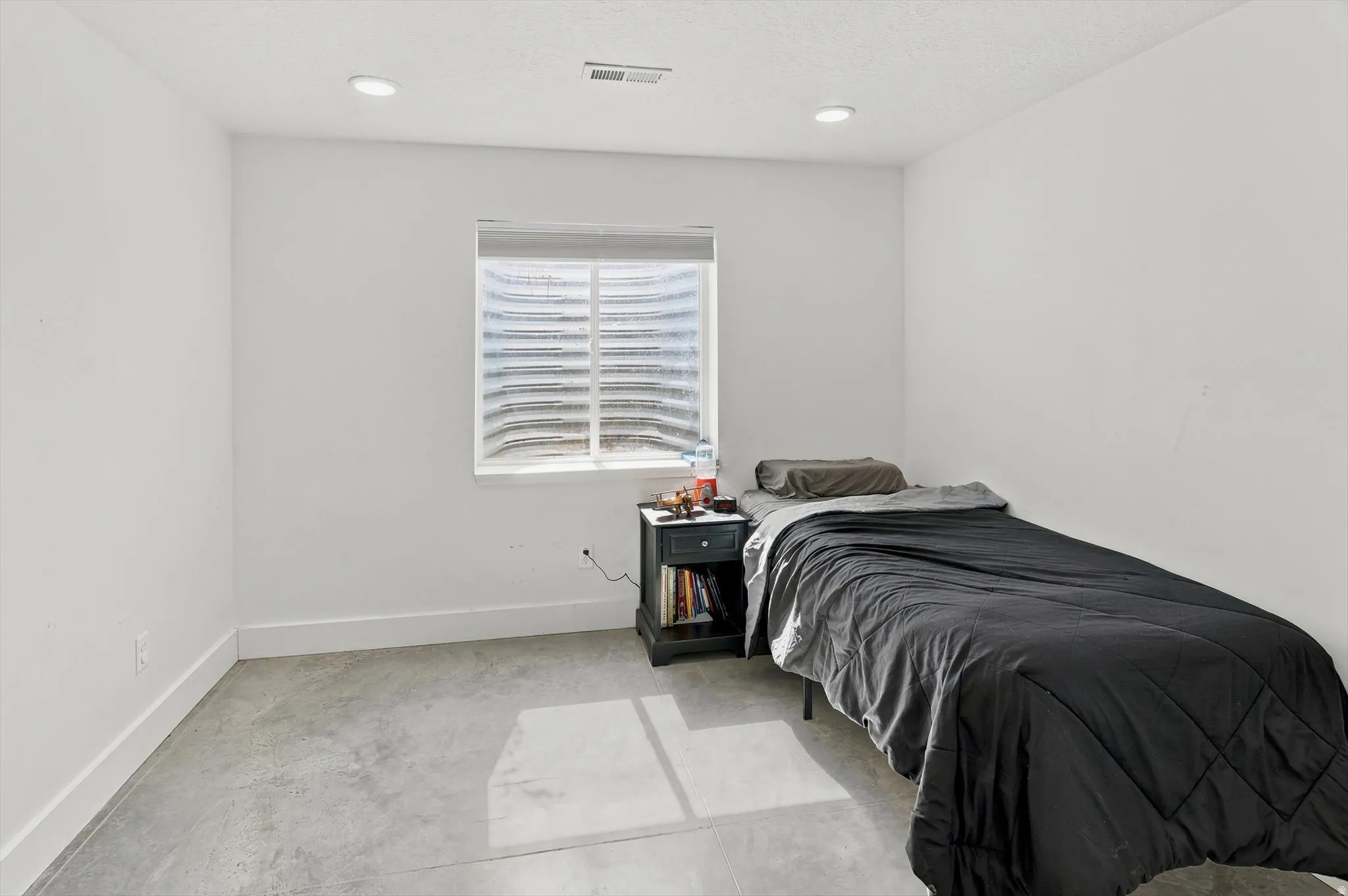 Bright room featuring a window with integrated blinds, recessed lighting, and a concrete floor