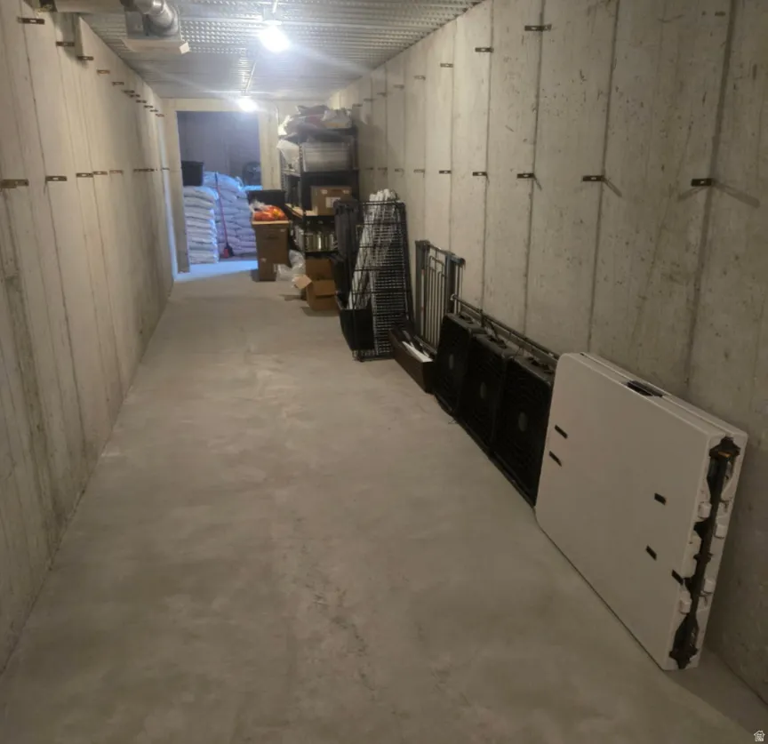Concrete flooring and walls define this utility corridor, featuring exposed ceiling joists and overhead lighting fixtures