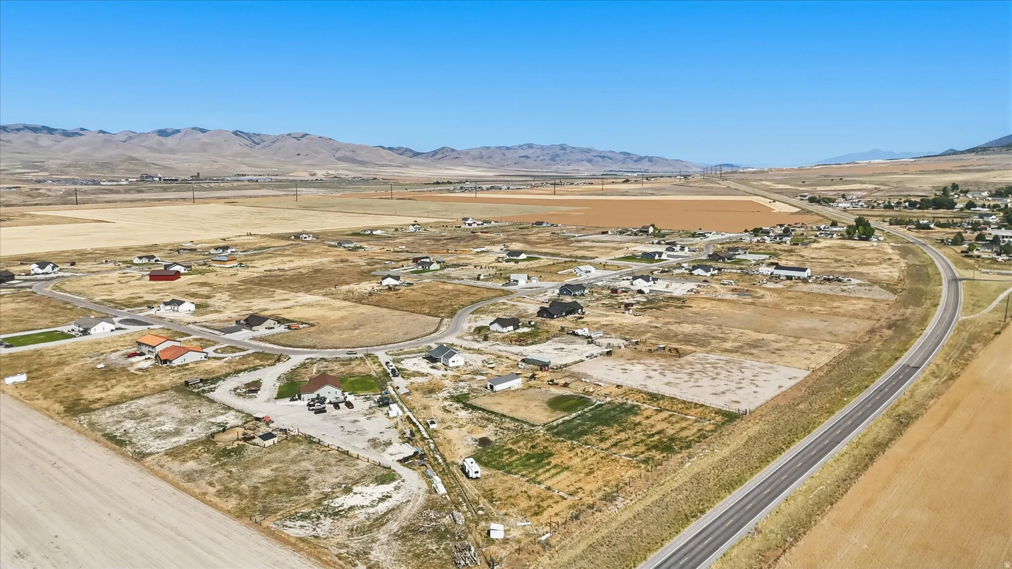 Expansive rural setting featuring scattered residential properties, a winding paved road, and distant mountains