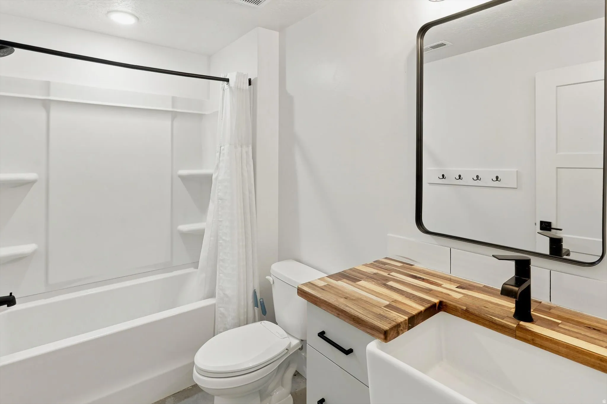 Bathroom featuring a white tub and shower surround with built-in shelving, a wood-finish countertop with an integrated sink, a dark bronze faucet, and a rectangular mirror with a dark bronze frame