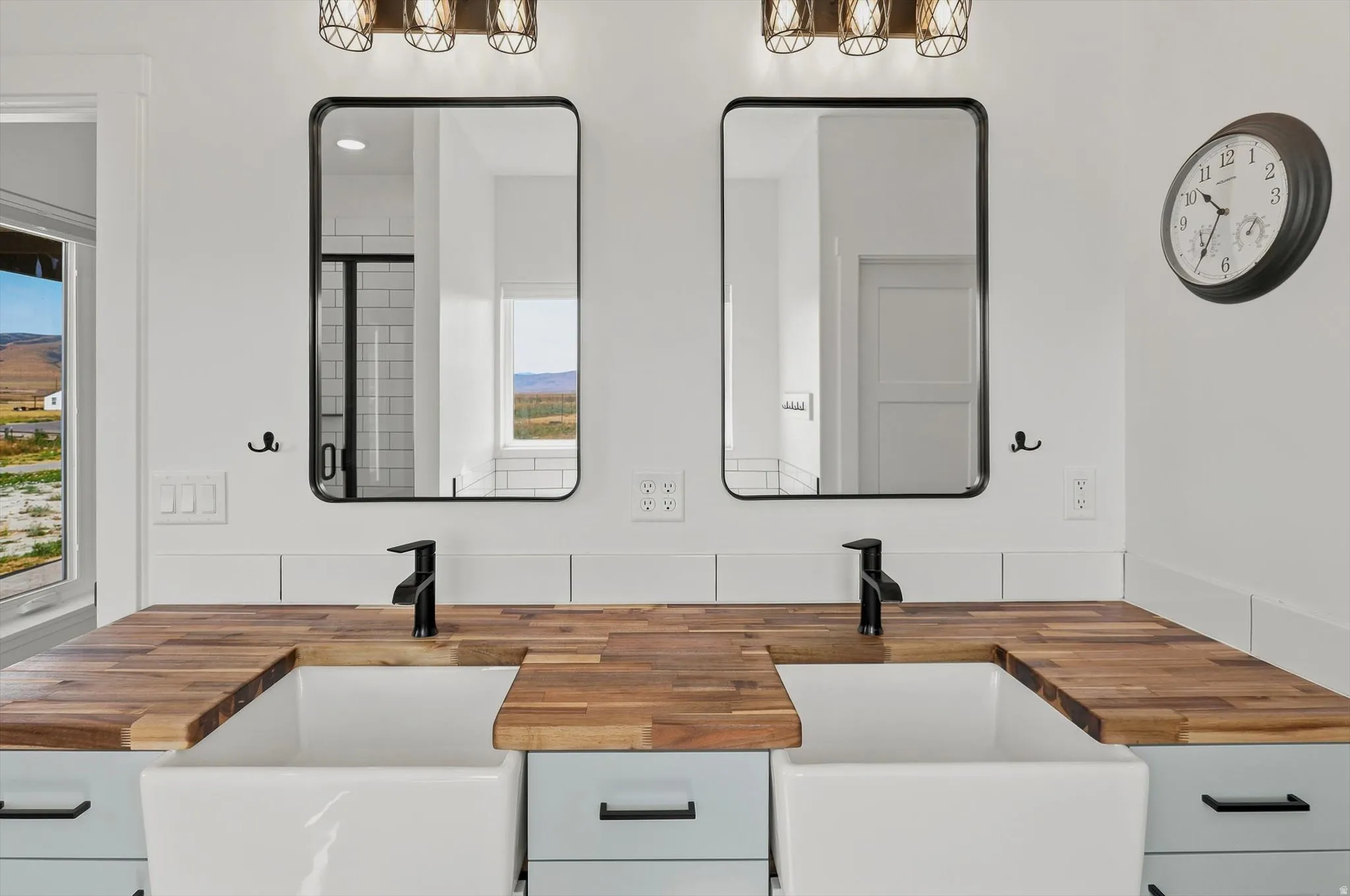 Dual farmhouse sinks set into a butcher block countertop, complemented by matte black faucets and rectangular mirrors with black frames