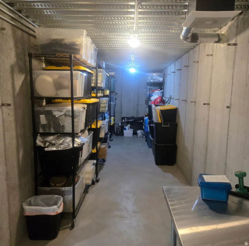 Concrete-walled storage area featuring a raw concrete floor, exposed metal ceiling joists, and overhead lighting