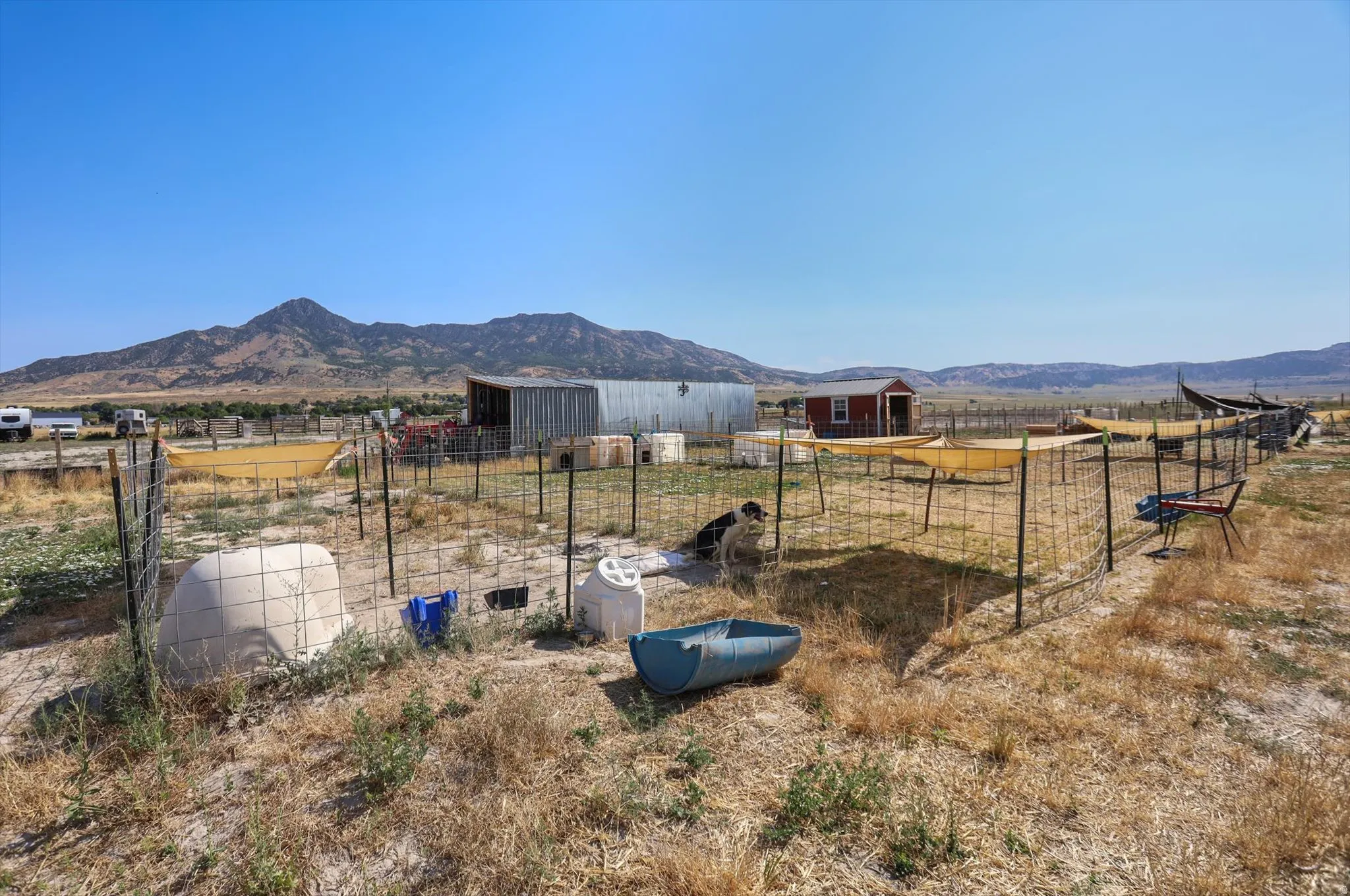 Expansive outdoor space featuring wire fencing, a red storage shed, and a large metal outbuilding