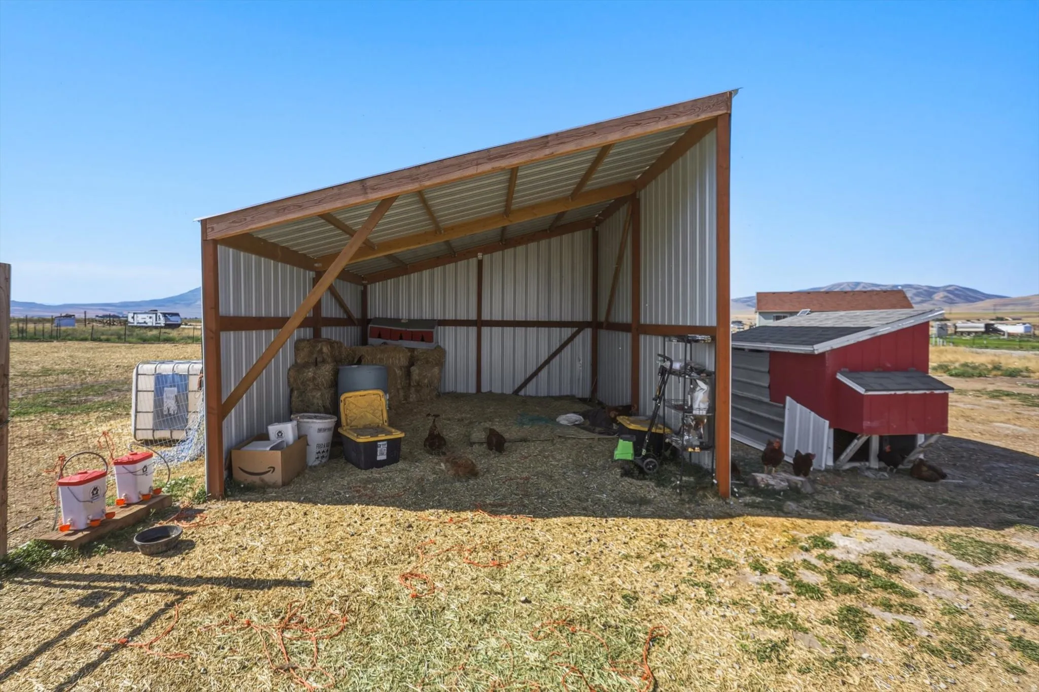 Open-sided barn structure featuring metal siding and a red-painted chicken coop with a black shingle roof