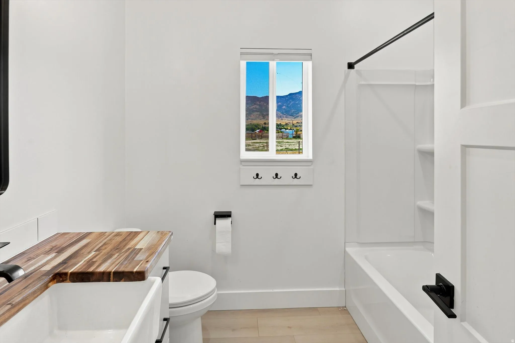 Bathroom featuring a white bathtub with a shower kit, a white toilet, and a vanity with a wood-finish countertop and an integrated white sink