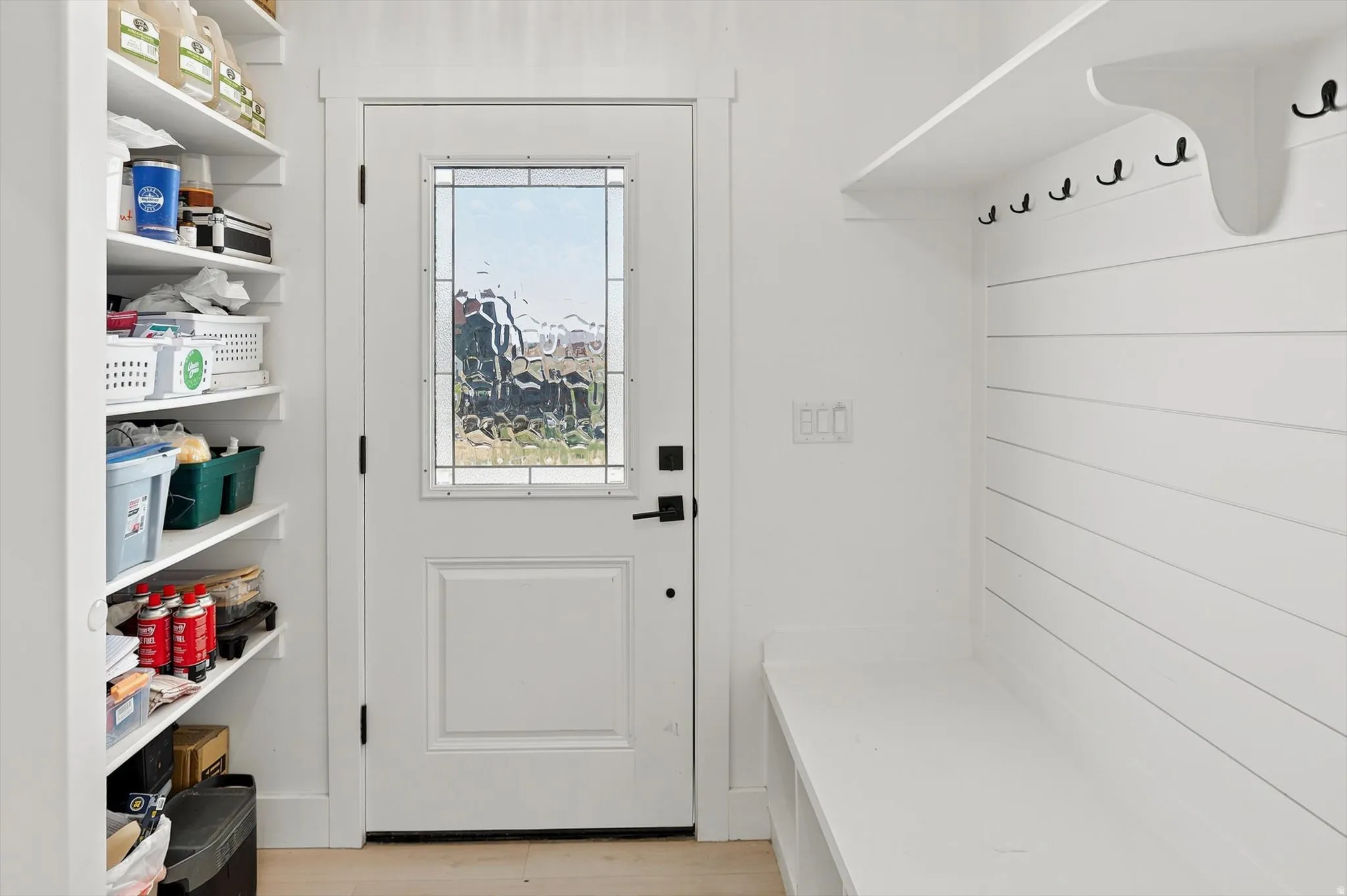Entryway featuring a white paneled door with decorative glass, built-in shelving, white shiplap wall paneling, and integrated bench seating with storage