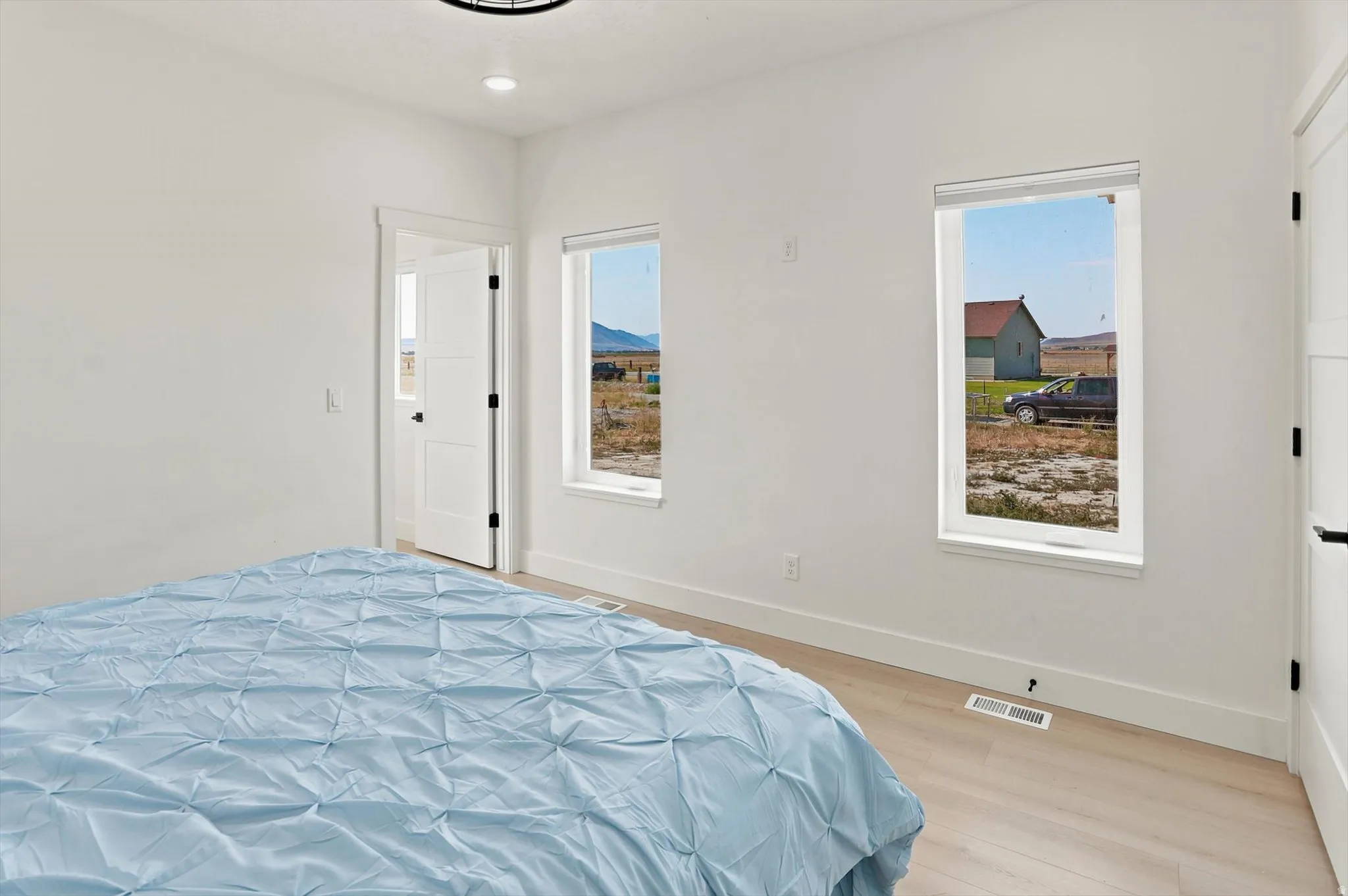 Bright bedroom featuring two windows, light wood-finish flooring, white walls, and a contemporary ceiling light fixture