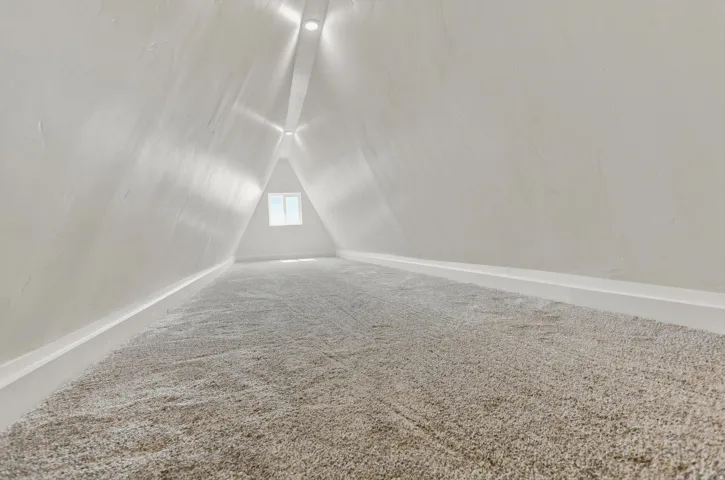 A-frame attic space featuring plush carpeting and a triangular window