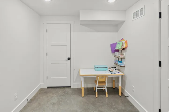 Spacious room featuring light gray flooring, recessed lighting, white trim, and a white three-panel door with black hardware