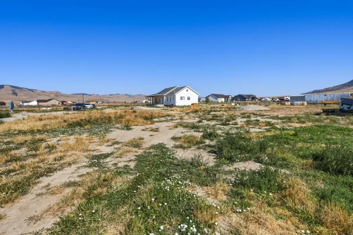 Expansive land parcel featuring a white ranch-style residence with a covered front porch, set against a distant mountain backdrop