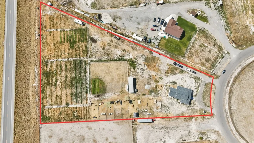 Expansive parcel featuring a two-story residence with a dark shingle roof, established fields, a paved road border, and direct road frontage