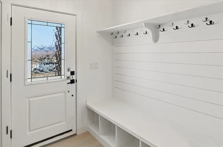 Entryway featuring a white door with decorative glass, shiplap wall paneling, built-in bench seating, multiple storage cubbies, and an array of coat hooks