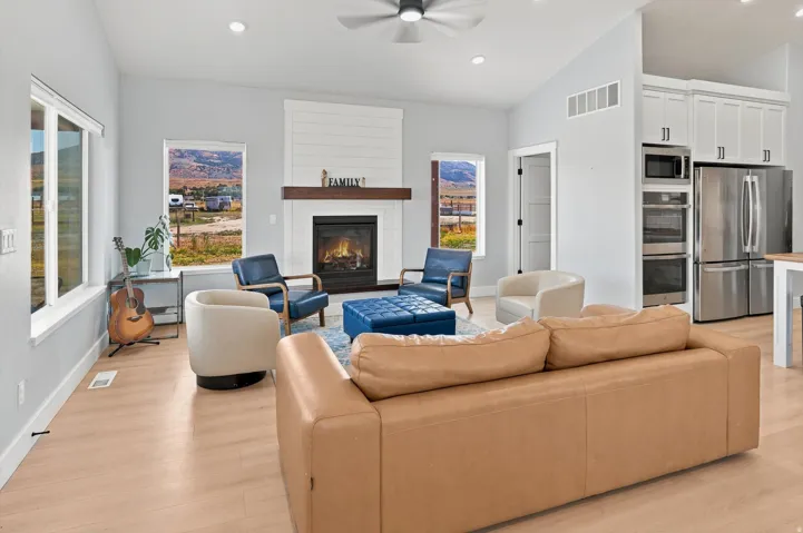 Open-concept living space featuring a fireplace with a wood mantel, light wood-finish flooring, recessed lighting, and a ceiling fan