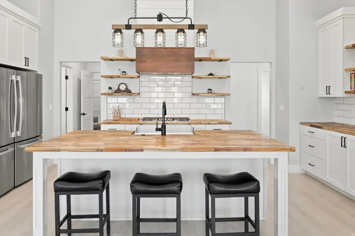 Kitchen featuring a large wood-finish island, white subway tile backsplash, a stainless steel refrigerator, white cabinetry, and a unique industrial-style chandelier