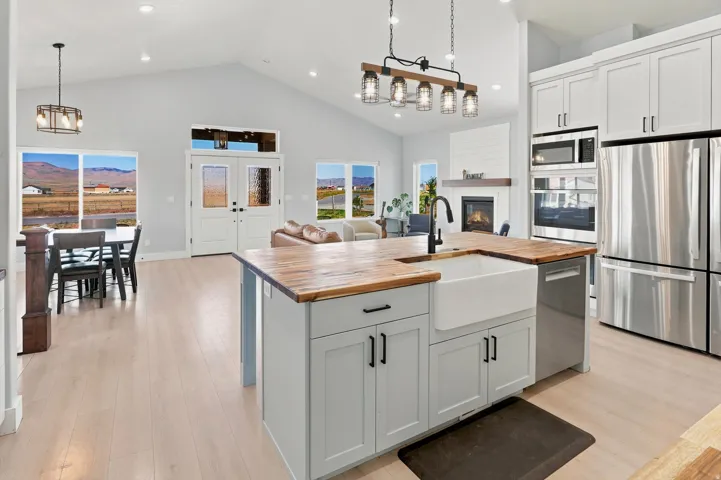Spacious open-concept kitchen featuring light-toned cabinetry, stainless steel appliances, a farmhouse sink, and wood-finish countertops
