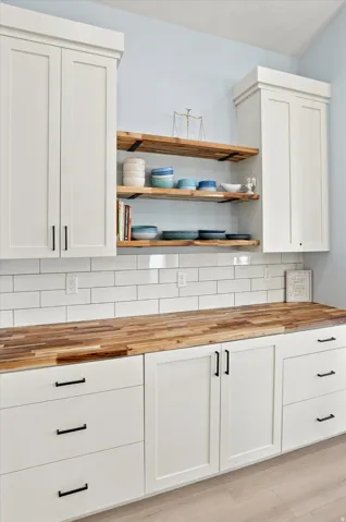 White shaker-style cabinetry with black hardware, butcher block countertops, subway tile backsplash, and open wood shelving