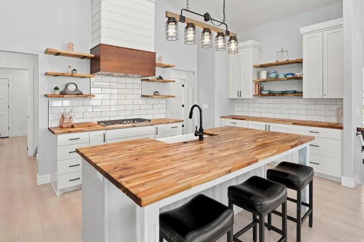 Kitchen featuring an expansive butcher block island with integrated sink and seating, white cabinetry with black hardware, and open wood shelving