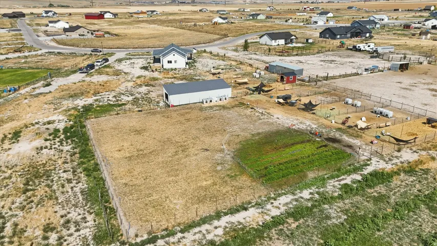 Expansive property featuring a large rectangular field, a structured garden plot, and a substantial outbuilding with a gray roof