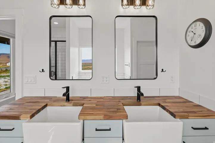 Dual farmhouse sinks set into a butcher block countertop, complemented by matte black faucets and rectangular mirrors with black frames