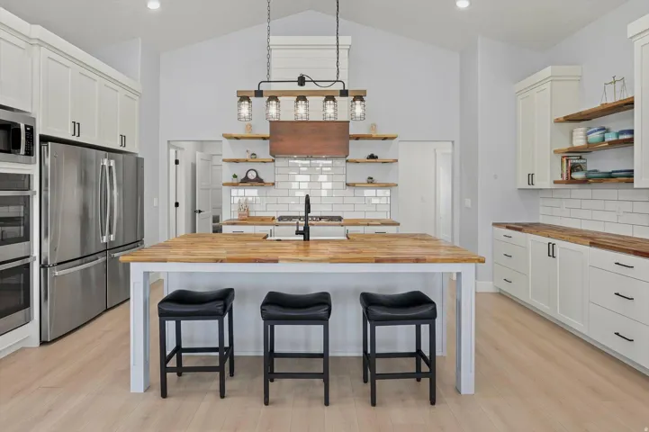 Spacious kitchen featuring an expansive center island with wood-finish countertop, white cabinetry with black hardware, wood-finish flooring, and vaulted ceiling