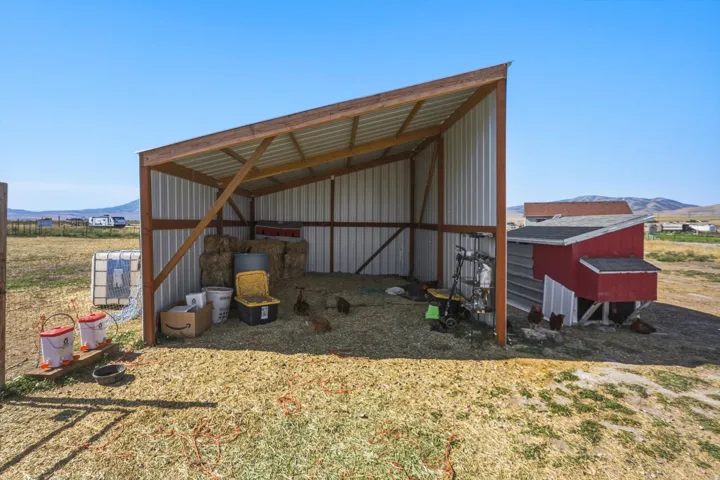 Open-sided barn structure featuring metal siding and a red-painted chicken coop with a black shingle roof