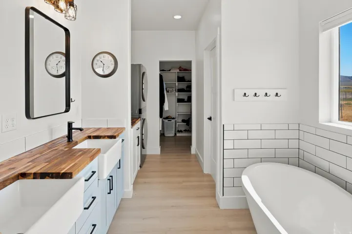 Spacious bathroom featuring a freestanding soaking tub, dual farmhouse sinks with wood-finish countertops, light wood-finish flooring, and a washer/dryer hookup