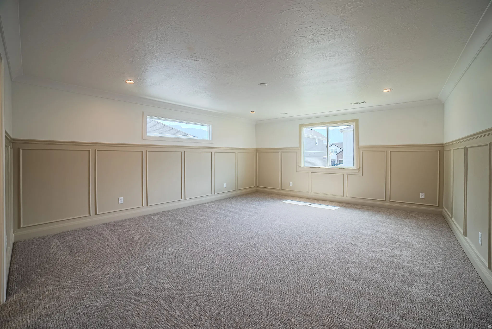 Spacious room featuring neutral carpeting, extensive wainscoting, recessed lighting, crown molding, and multiple windows