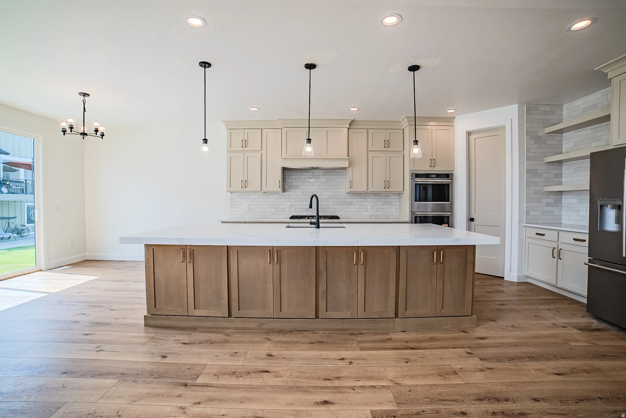 Spacious kitchen featuring a large island with under-counter storage, light-toned cabinetry, built-in double ovens, and wood-finish flooring