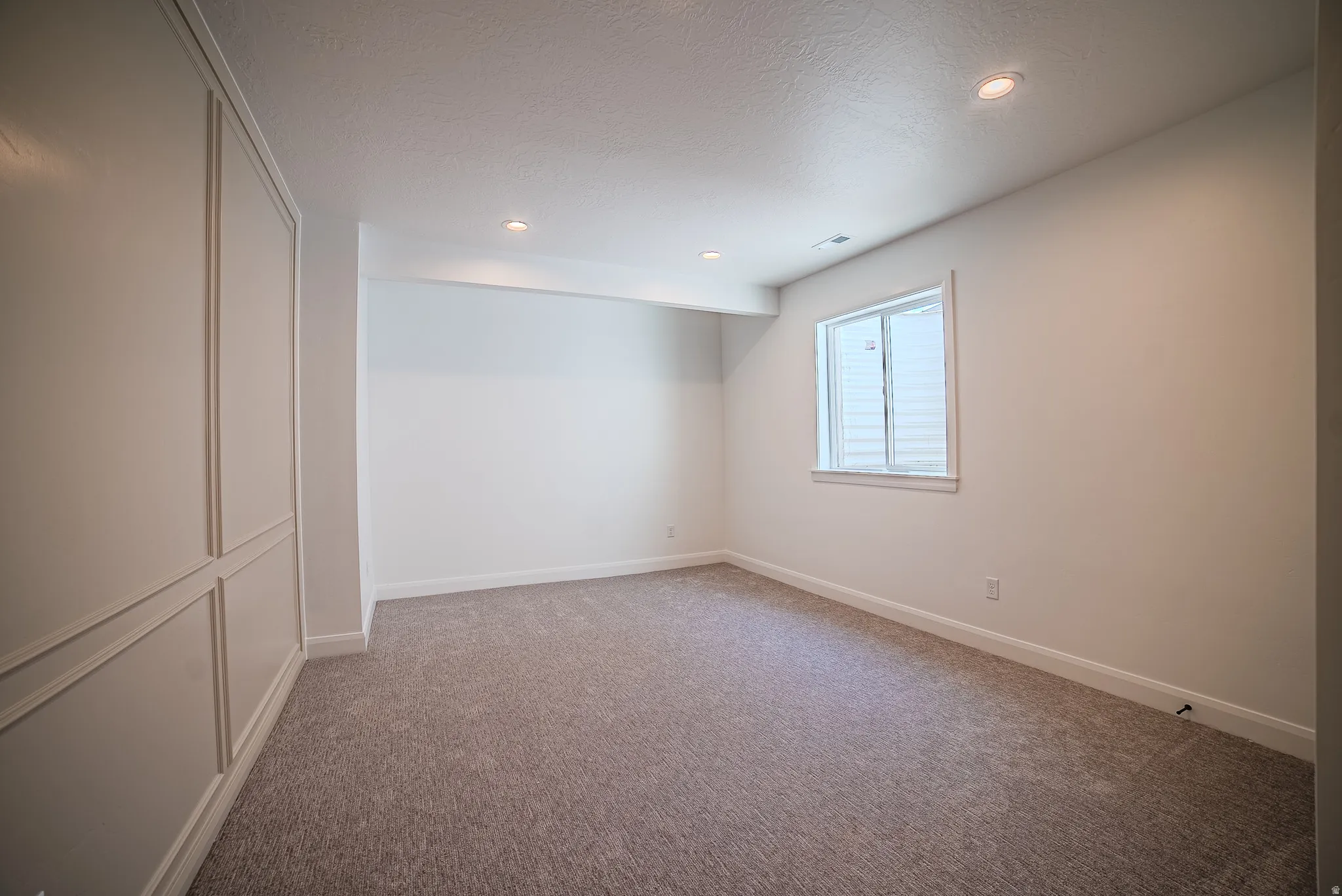 Carpeted room featuring recessed lighting, a single window, and wainscoting on one wall