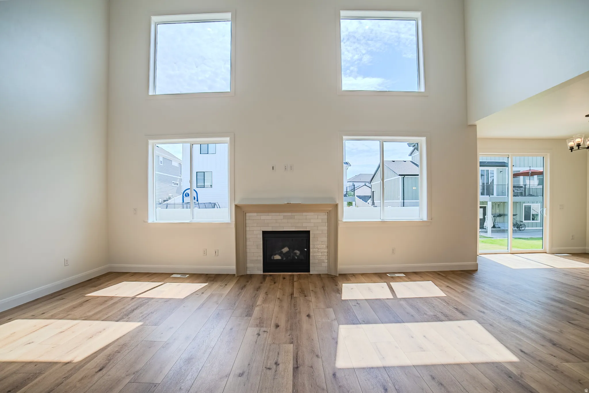 Spacious living area featuring high ceilings, wood-finish flooring, a contemporary fireplace with a tiled surround and wood mantel, large upper and lower windows, and a glass sliding door