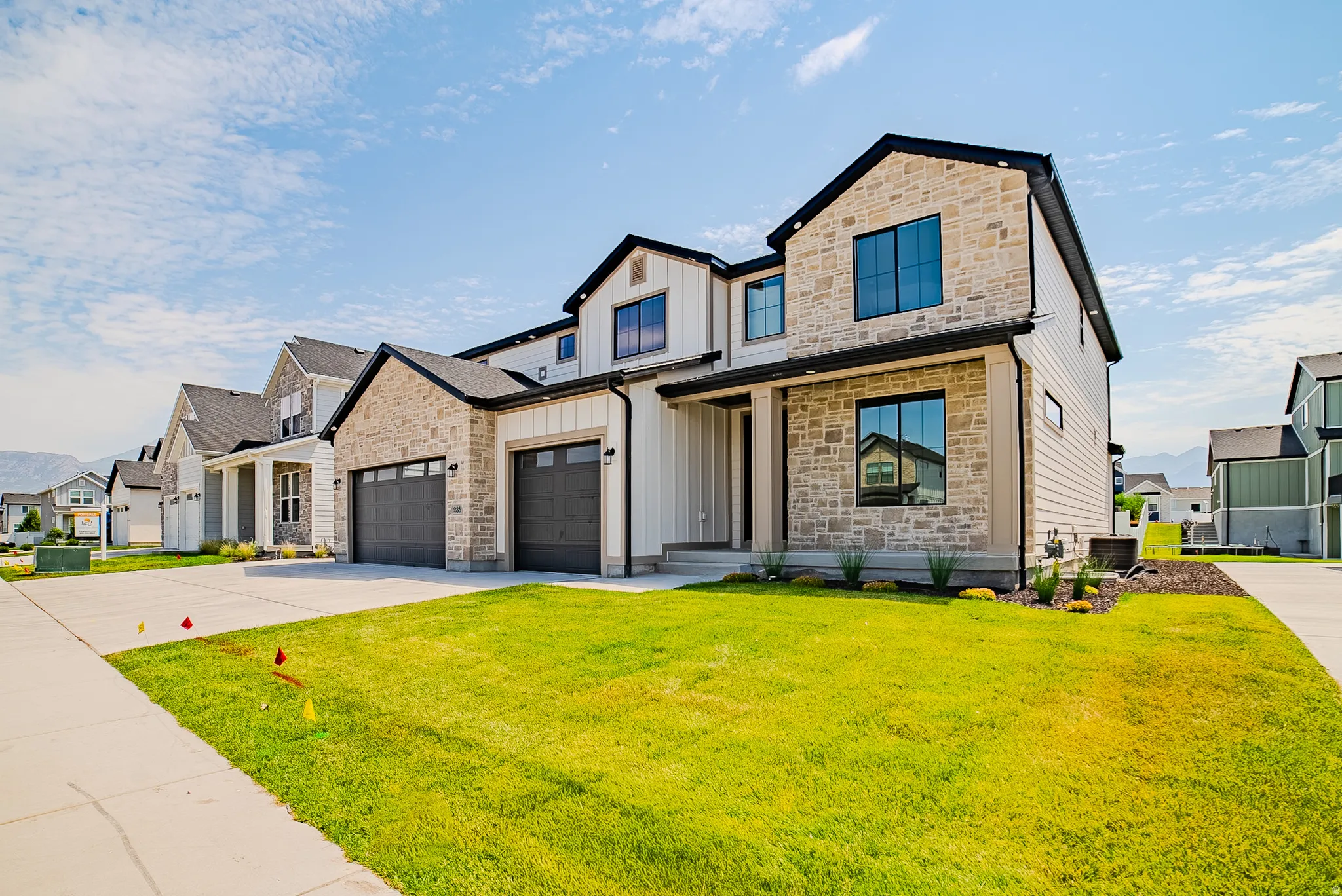 Contemporary exterior featuring stone veneer, white vertical and horizontal siding, black trim, and a two-car garage