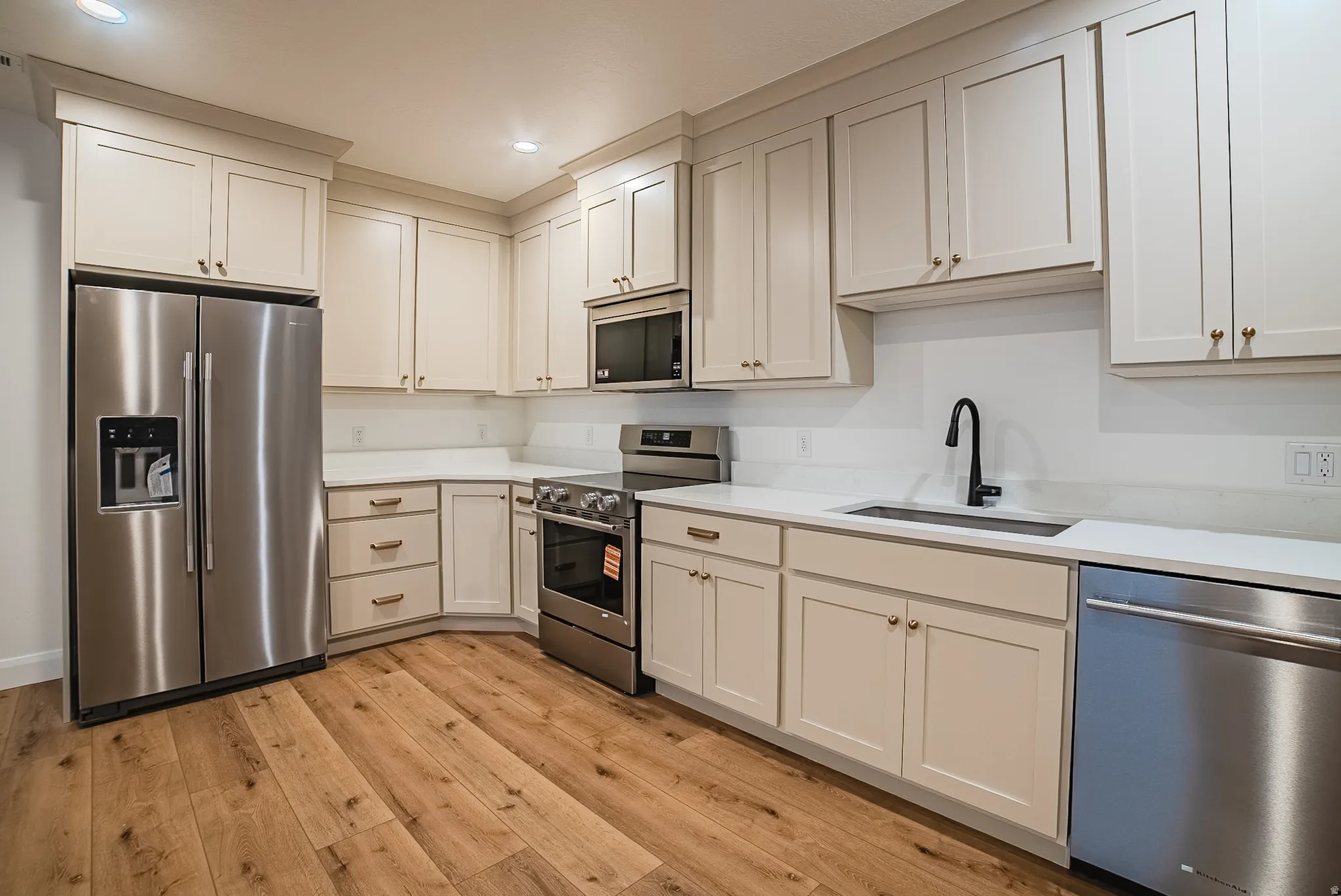 Kitchen featuring wood-finish flooring, light-toned cabinetry, stainless steel appliances, white countertops, and a matte black faucet