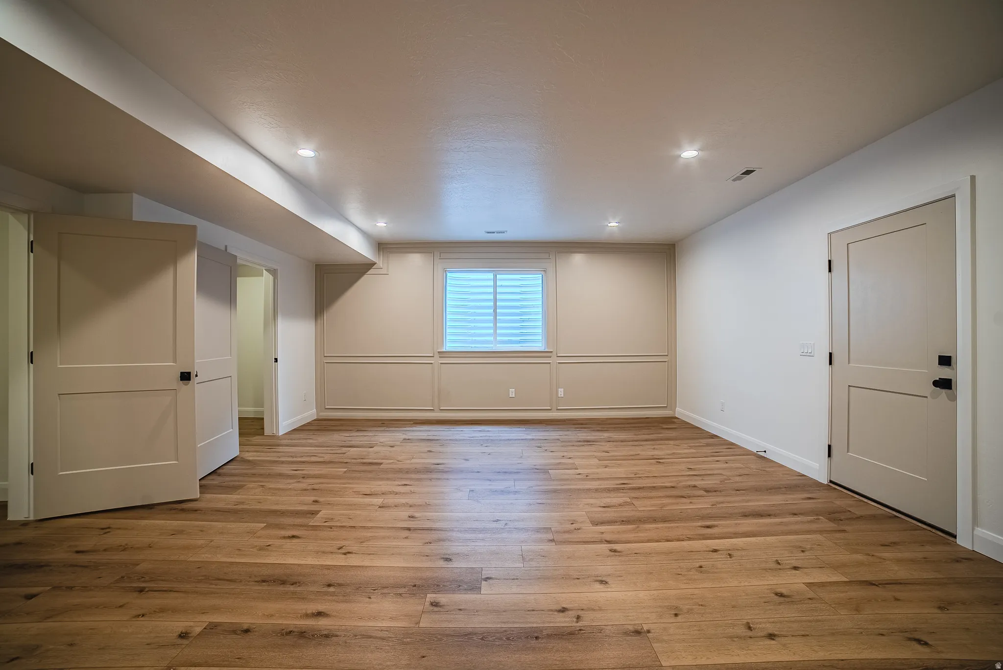 Spacious lower-level room featuring wood-finish flooring, recessed lighting, and neutral wall tones