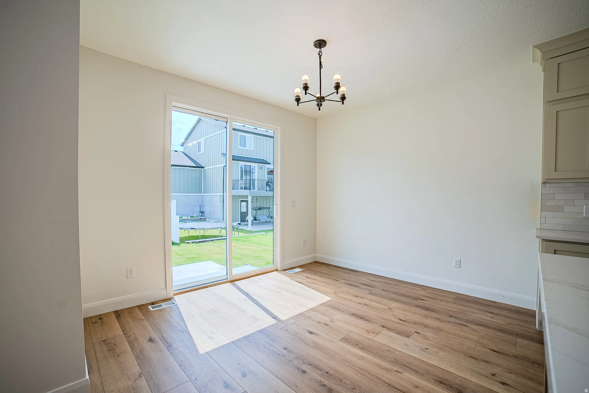 Spacious interior featuring wood-finish flooring, a contemporary chandelier, and a sliding glass door opening to the backyard