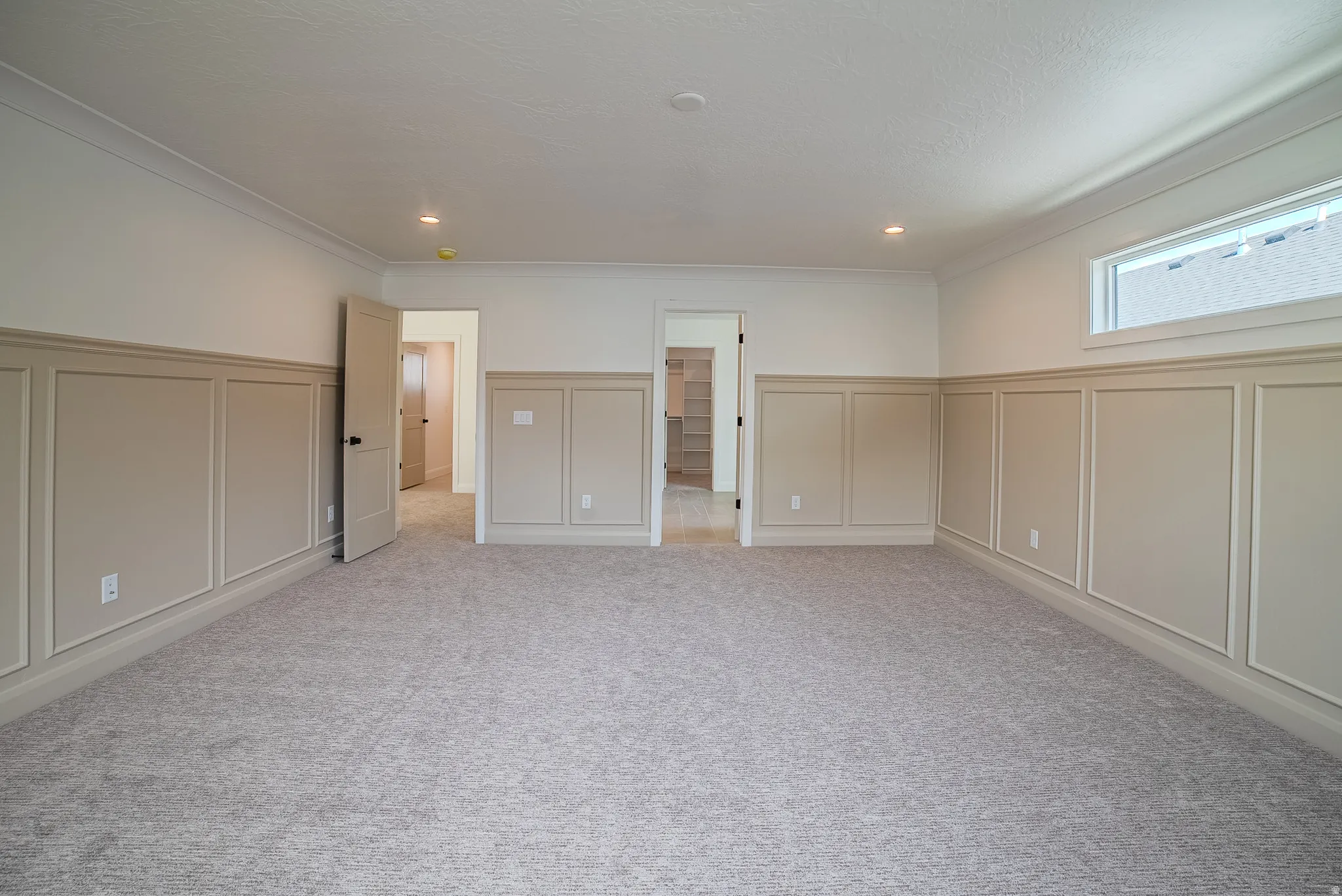 Spacious room featuring neutral carpeting, wainscoting paneling, crown molding, a transom window, and recessed lighting