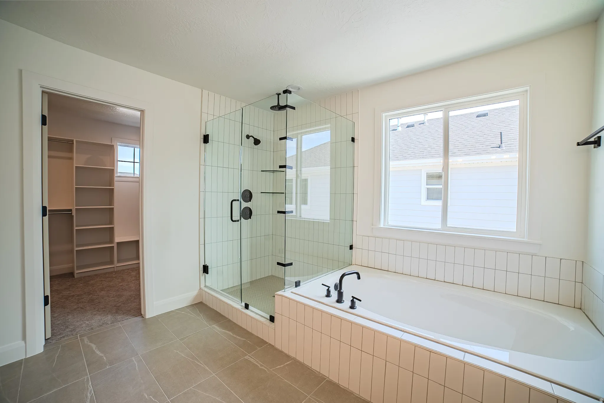 Bathroom featuring a glass-enclosed shower with black fixtures, a white soaking tub with black fixtures, subway tile surround, and large window
