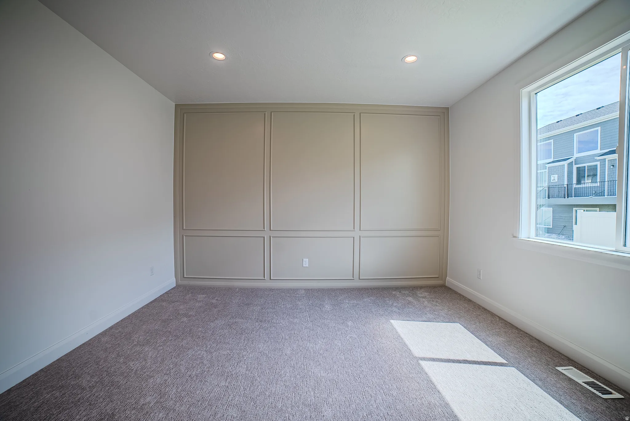 Spacious room featuring a decorative accent wall with panel molding, neutral-toned carpeting, and recessed ceiling lighting