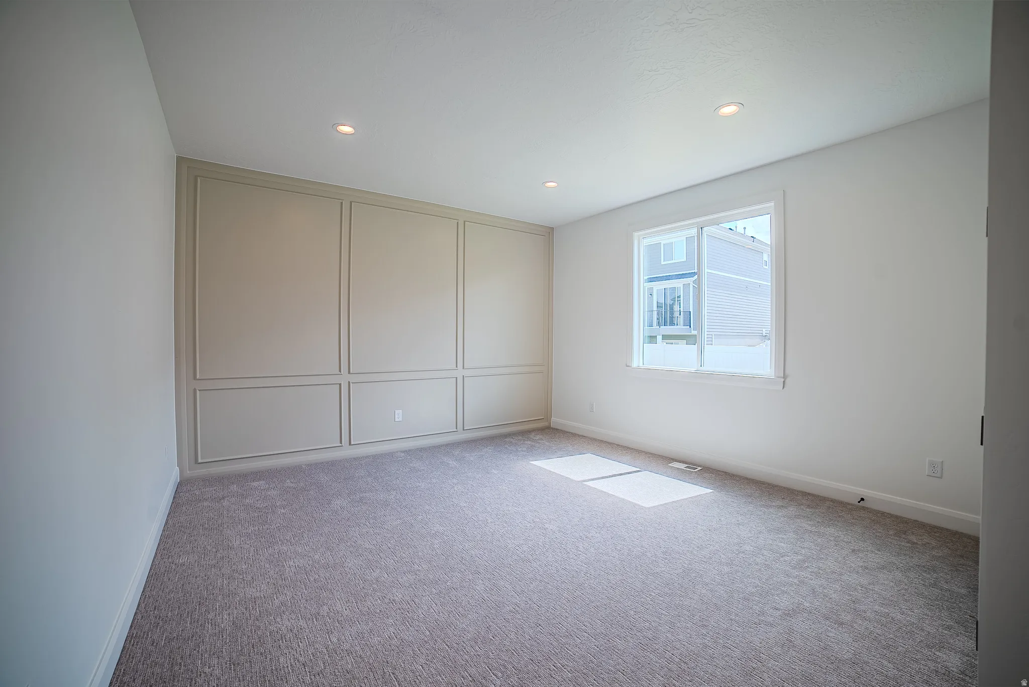 Spacious room featuring accent wall with panel molding, recessed lighting, neutral carpeting, and a large window