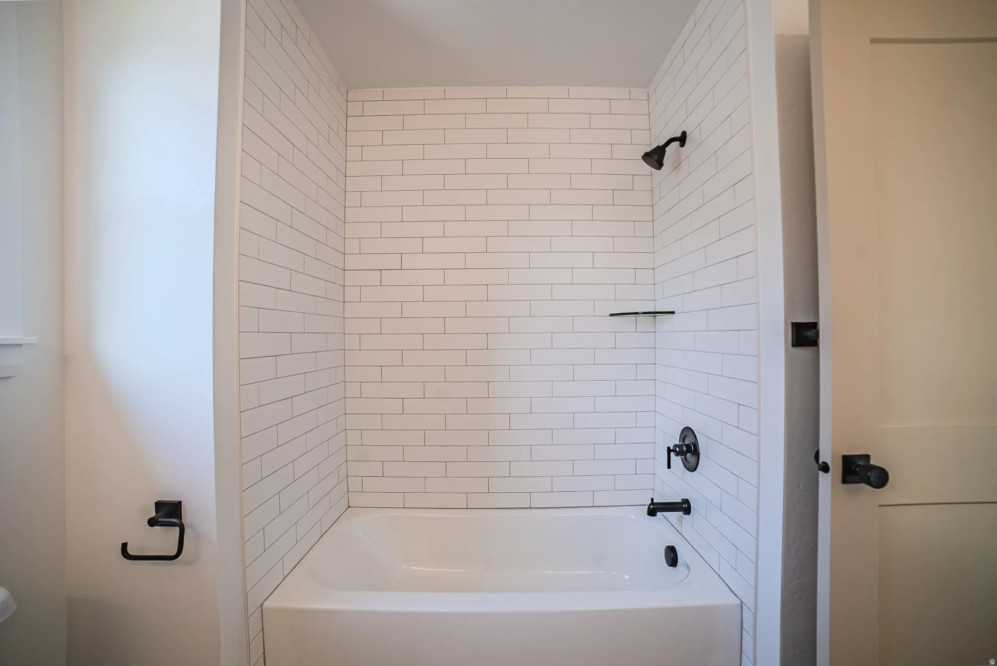 Bathtub and shower combination featuring white subway tile surround, matte black fixtures, and an integrated shelf