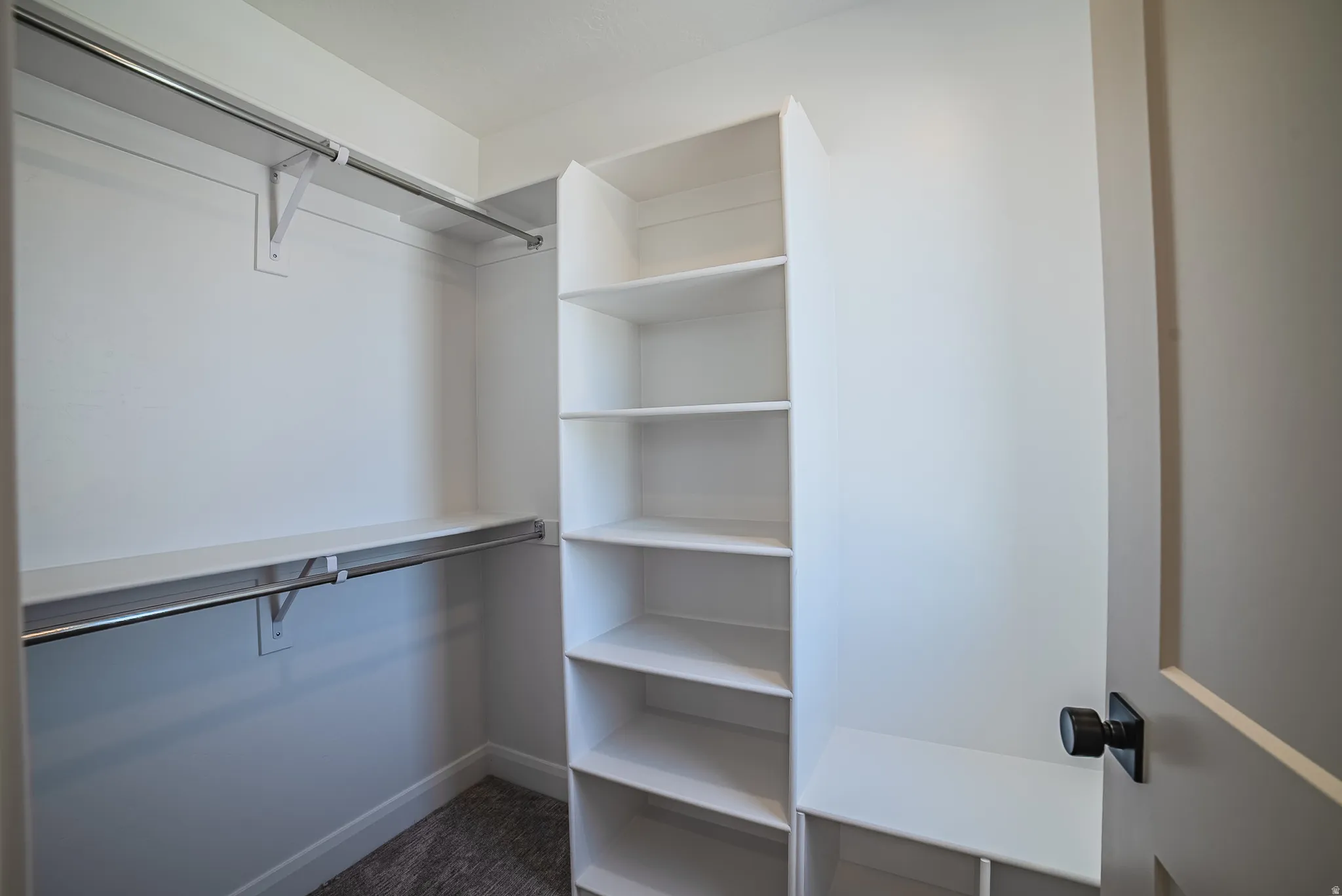 Walk-in closet featuring built-in shelving, two hanging rods, and a door with matte black hardware
