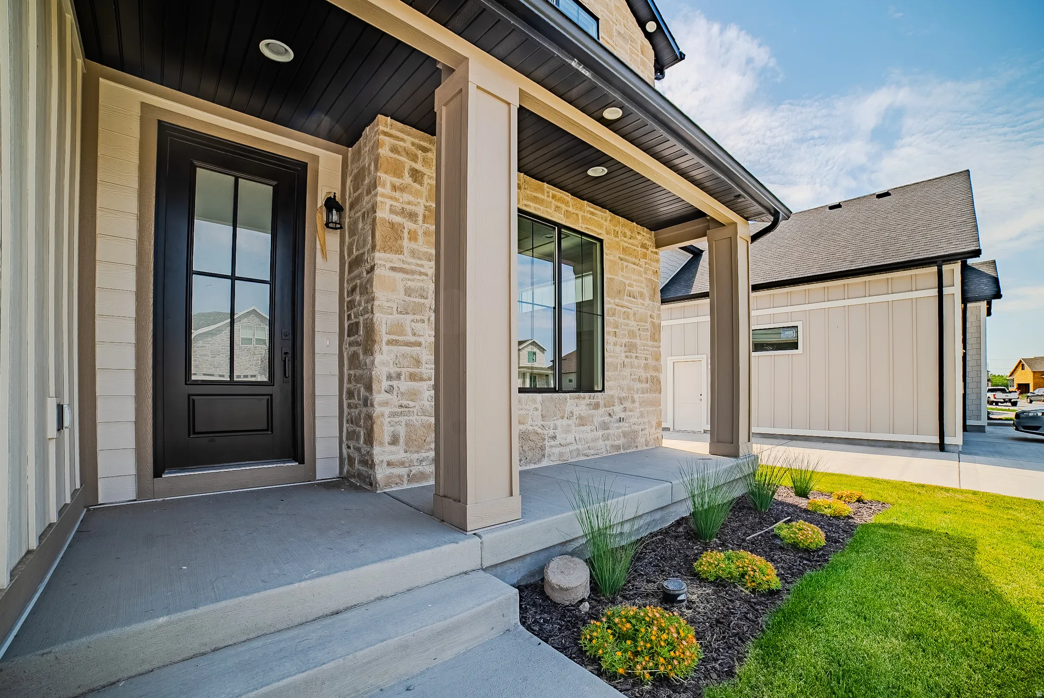 Inviting entryway featuring a dark-framed door with glass panels, textured stone cladding, and horizontal siding