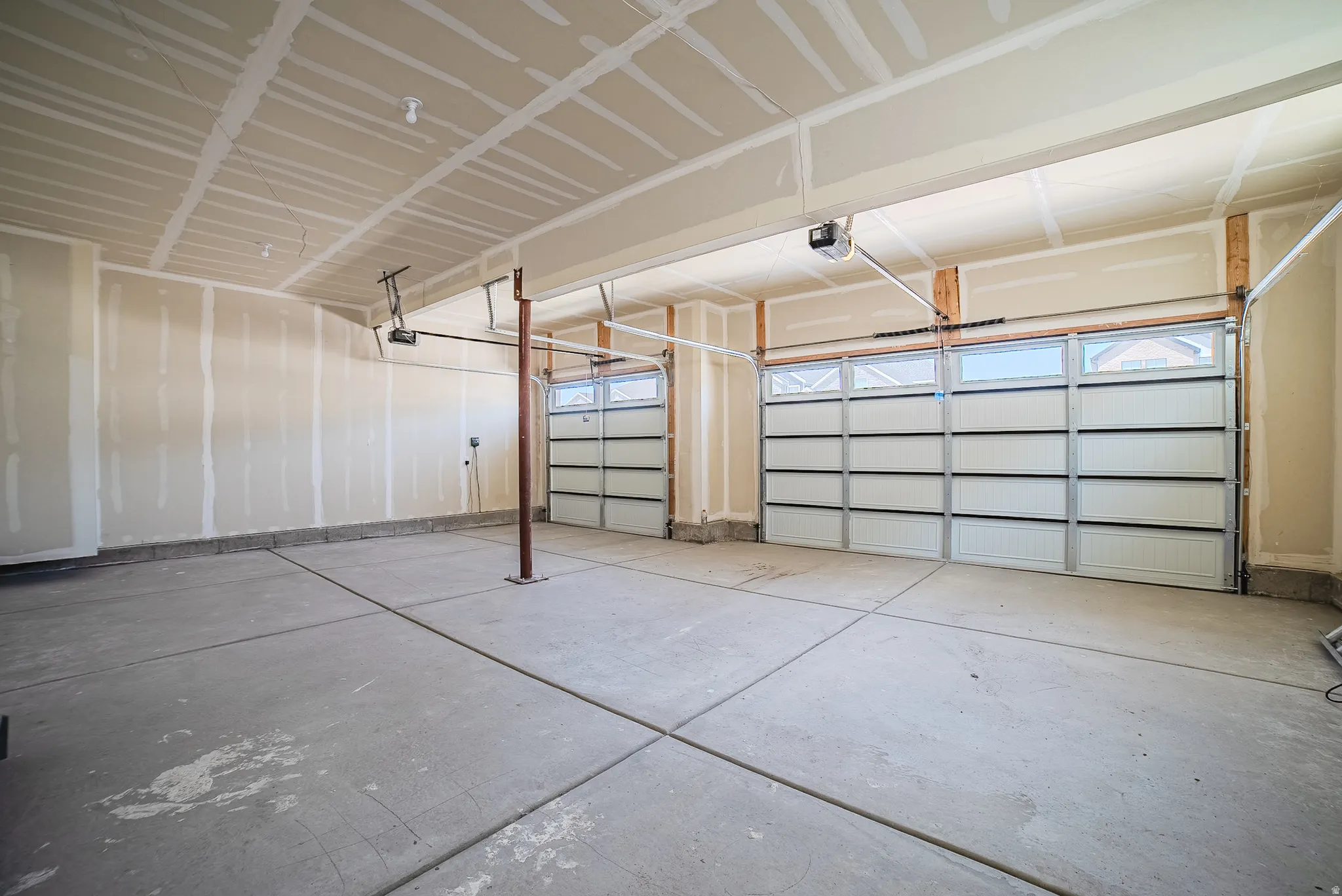 Two-bay garage with concrete flooring, two overhead doors featuring upper window panels, and exposed ceiling joists