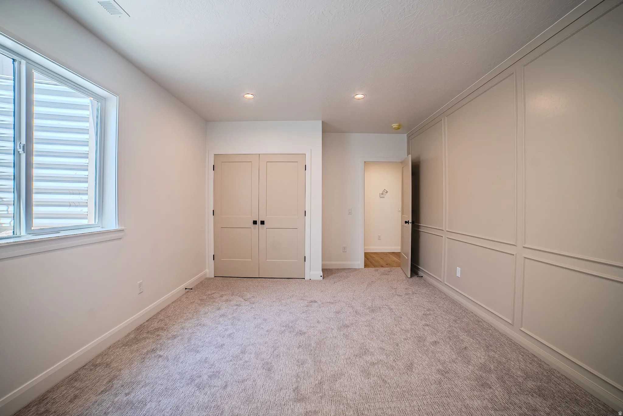 Spacious room with plush carpeting, a large window, a paneled accent wall, recessed lighting, and double bi-fold doors